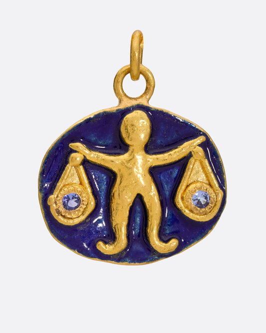 A deep blue enamel and high karat gold pendant with a Libra icon holding tanzanite scales.