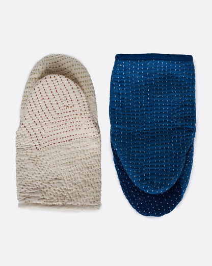 A pair of hand stitched oven mitts; one blue and one ivory. Shown lying flat from the back.