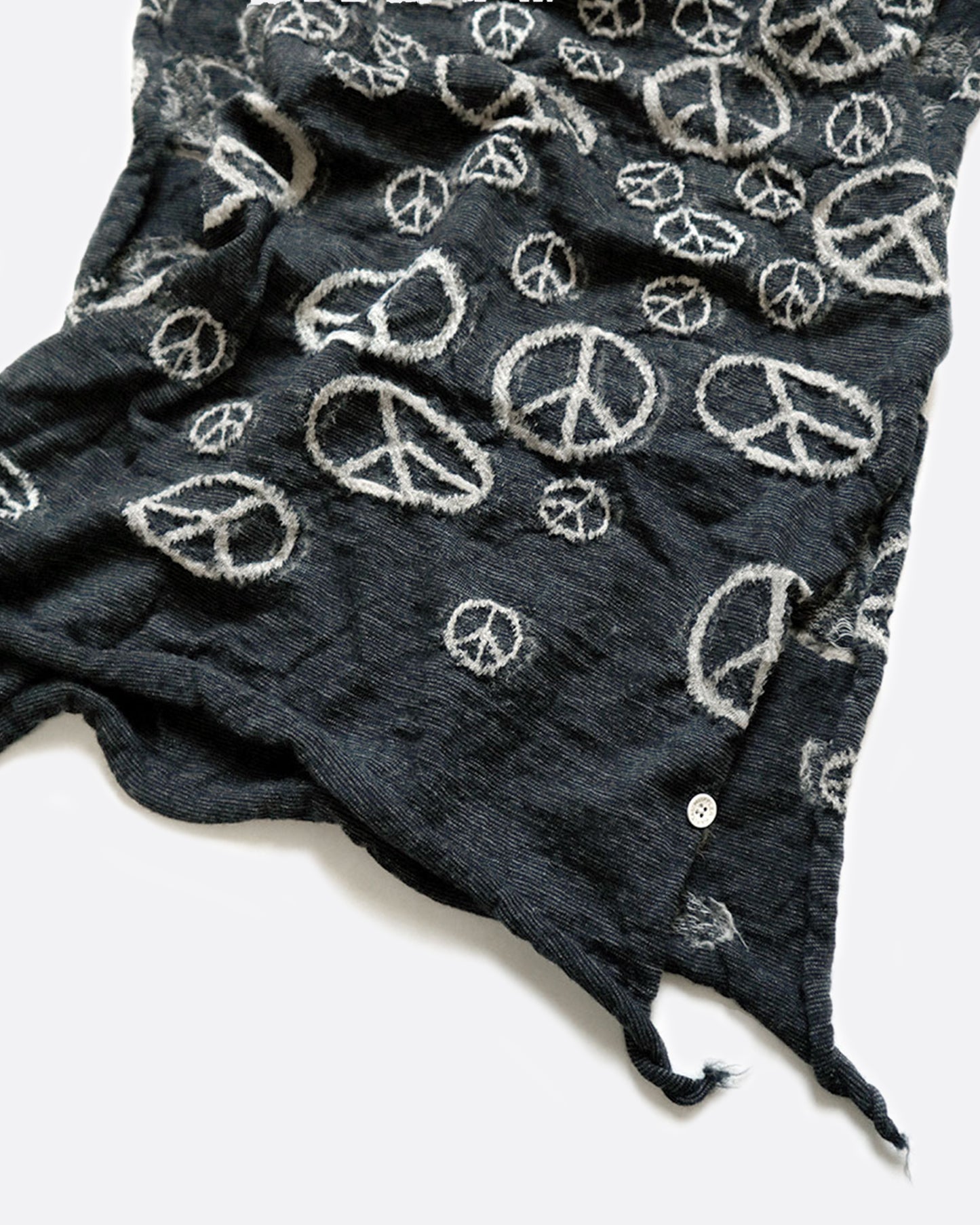 A close up of the ends of a black wool scarf with white peace signs.