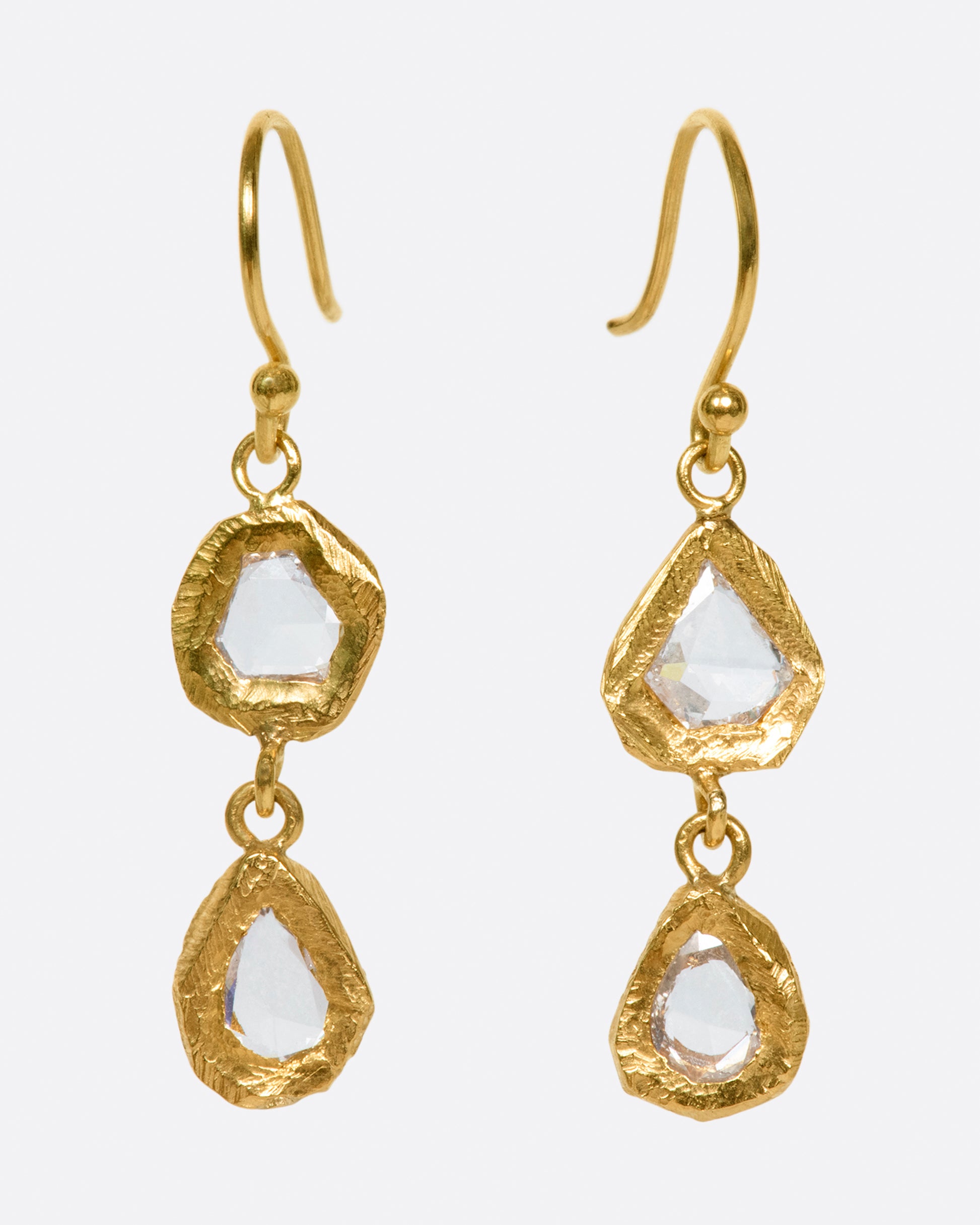 A pair of slightly asymmetrical diamond drop earrings with two diamonds set in hand carved bezels on each earring.