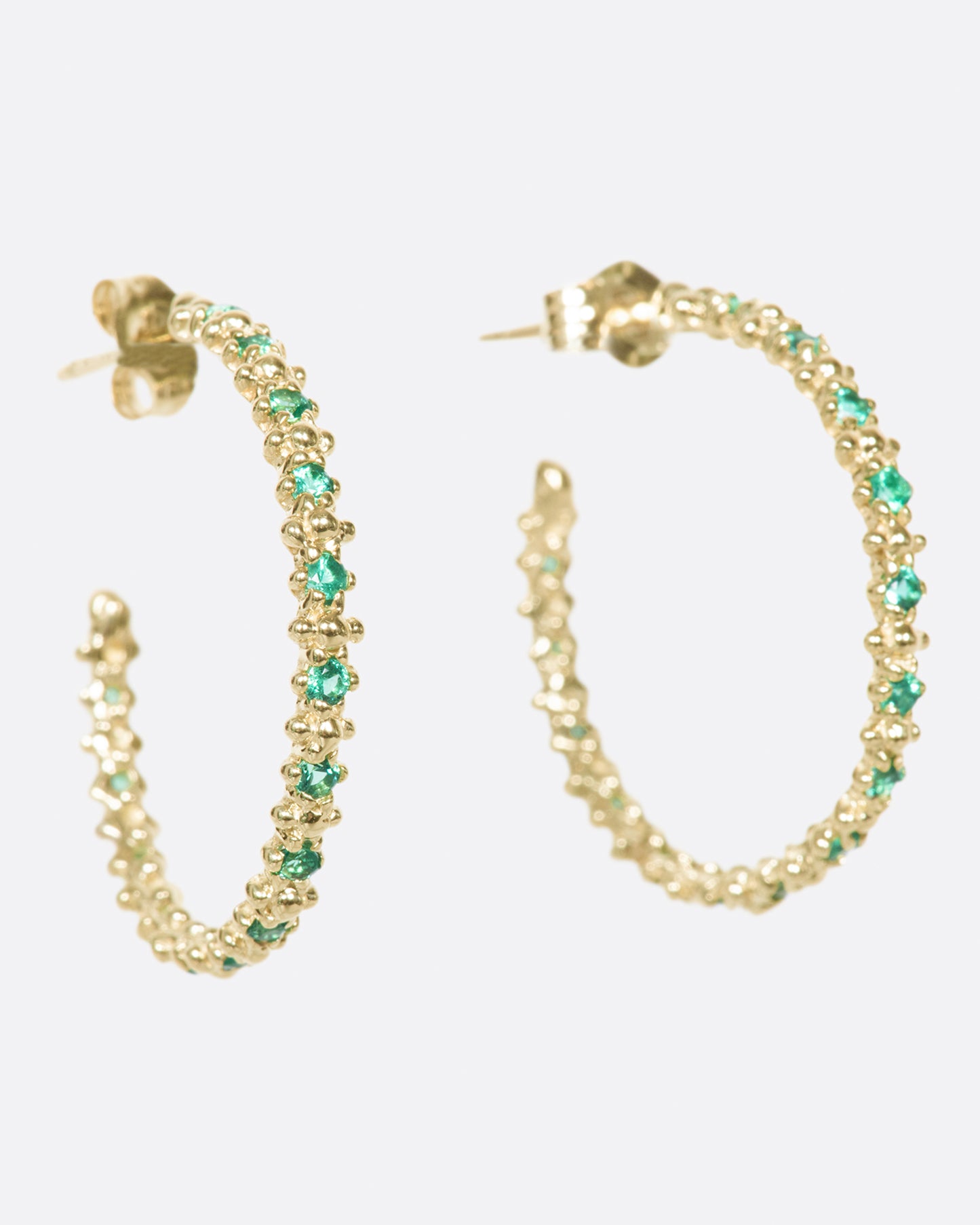 A pair of textured hoop earrings with emeralds dotted throughout.