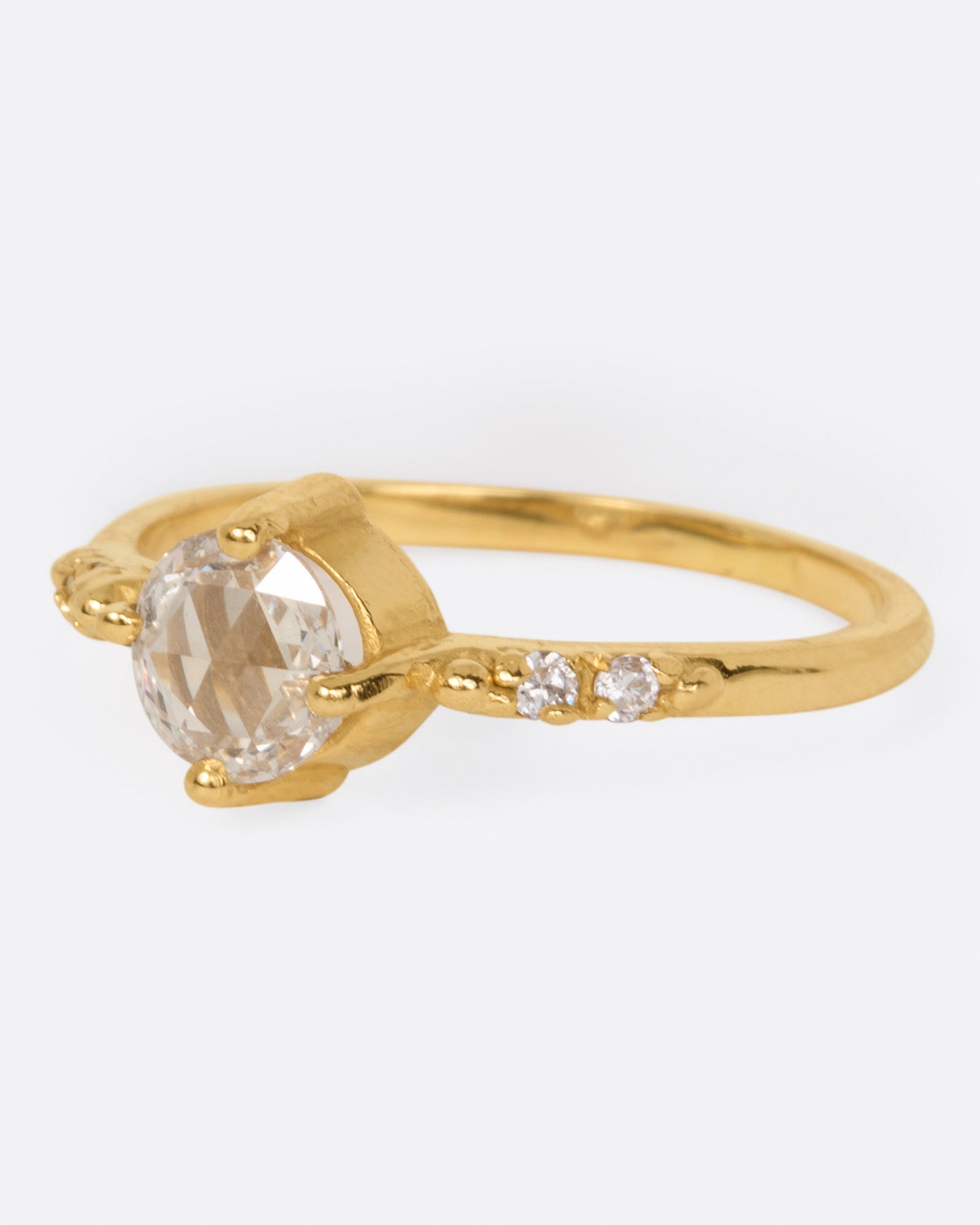 A yellow gold ring with a prong set rose cut diamond at the center and two diamonds on either side, shown from the side.