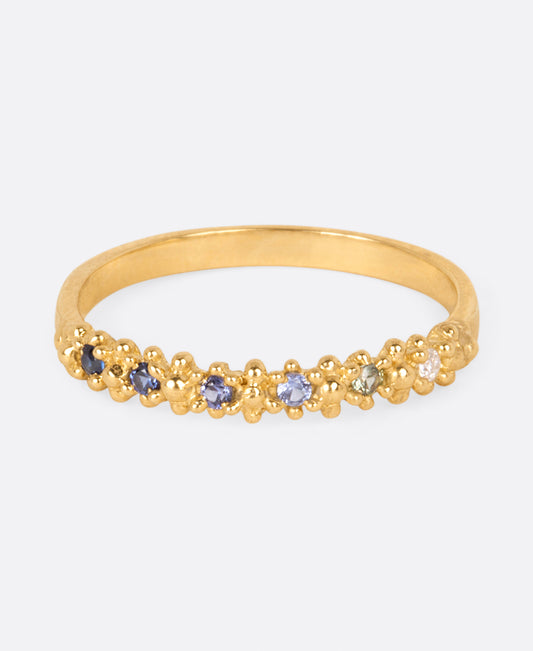 A textured yellow gold band with six sapphires in ombré order from white to dark blue, shown from the front.