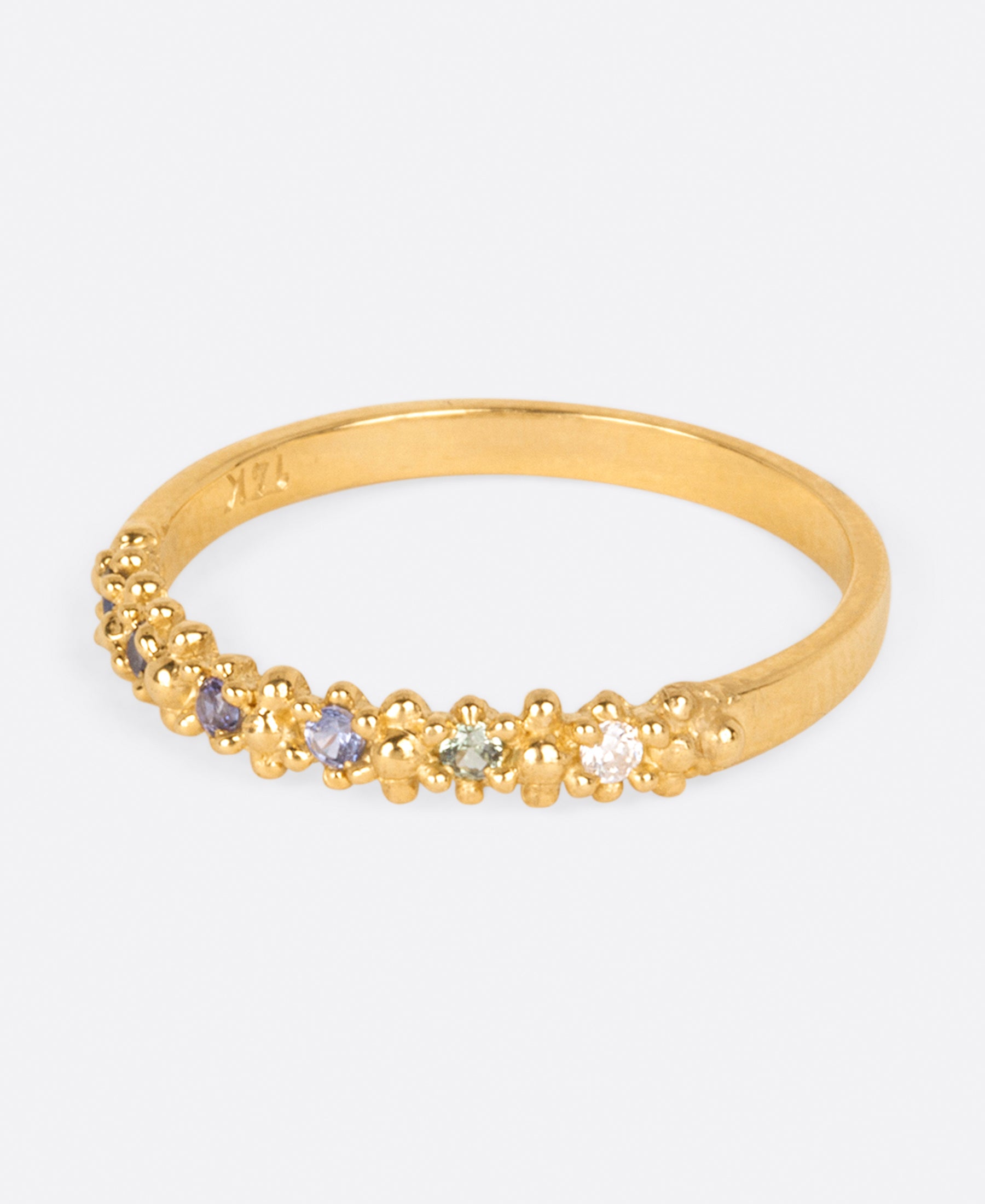 A textured yellow gold band with six sapphires in ombré order from white to dark blue, shown from the side.