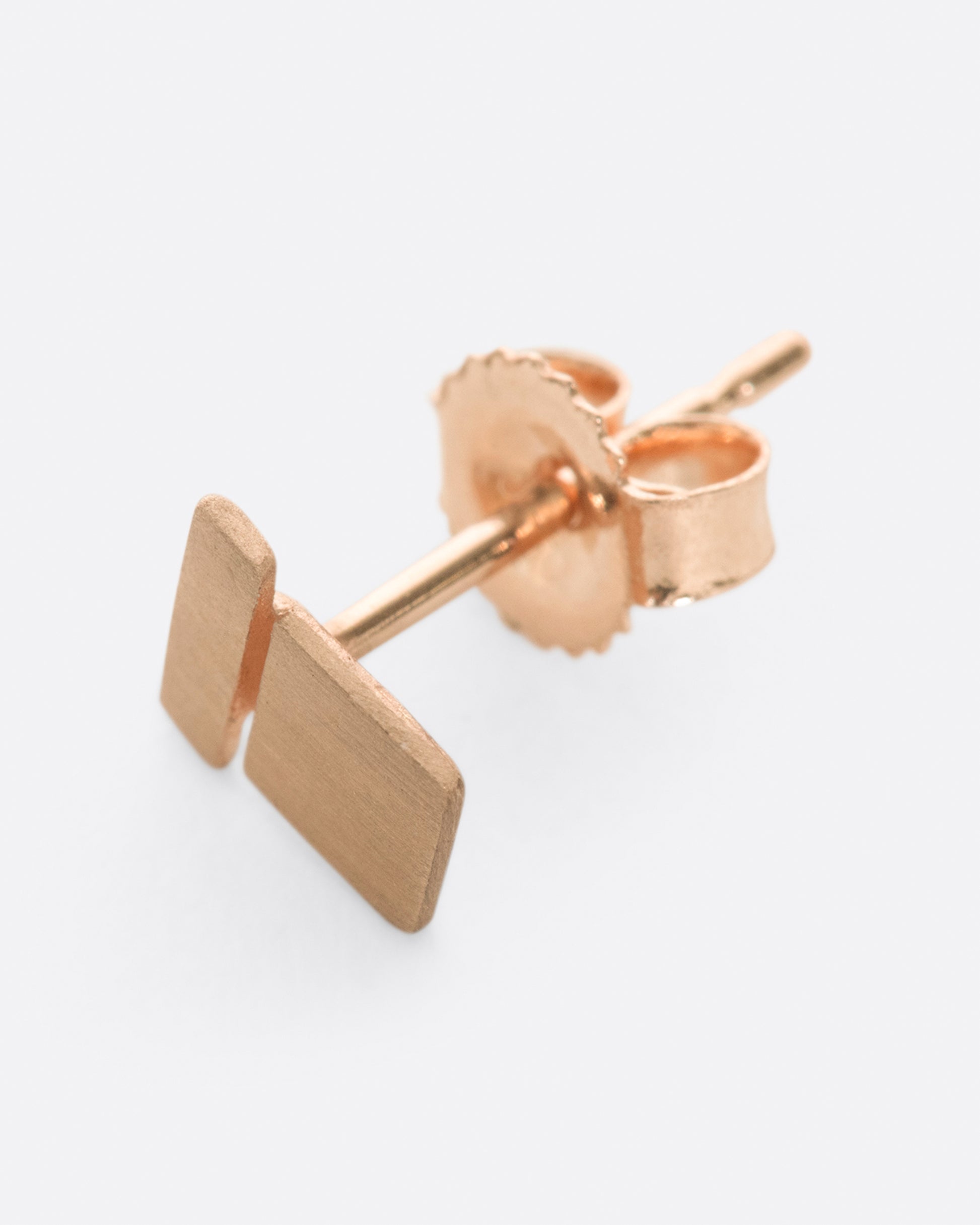 A matte rose gold geometric stud earring with a square stacked on a bar.