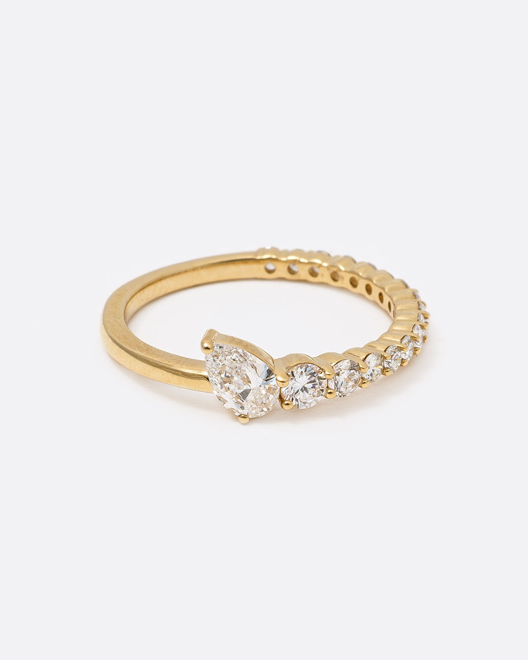 14k yellow gold ring with graduated white diamonds halfway around and one pear shaped white diamond by Selin Kent, from the front.