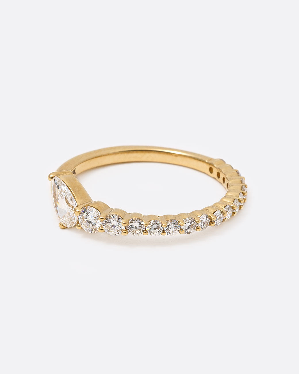 14k yellow gold ring with graduated white diamonds halfway around and one pear shaped white diamond by Selin Kent, from the side.