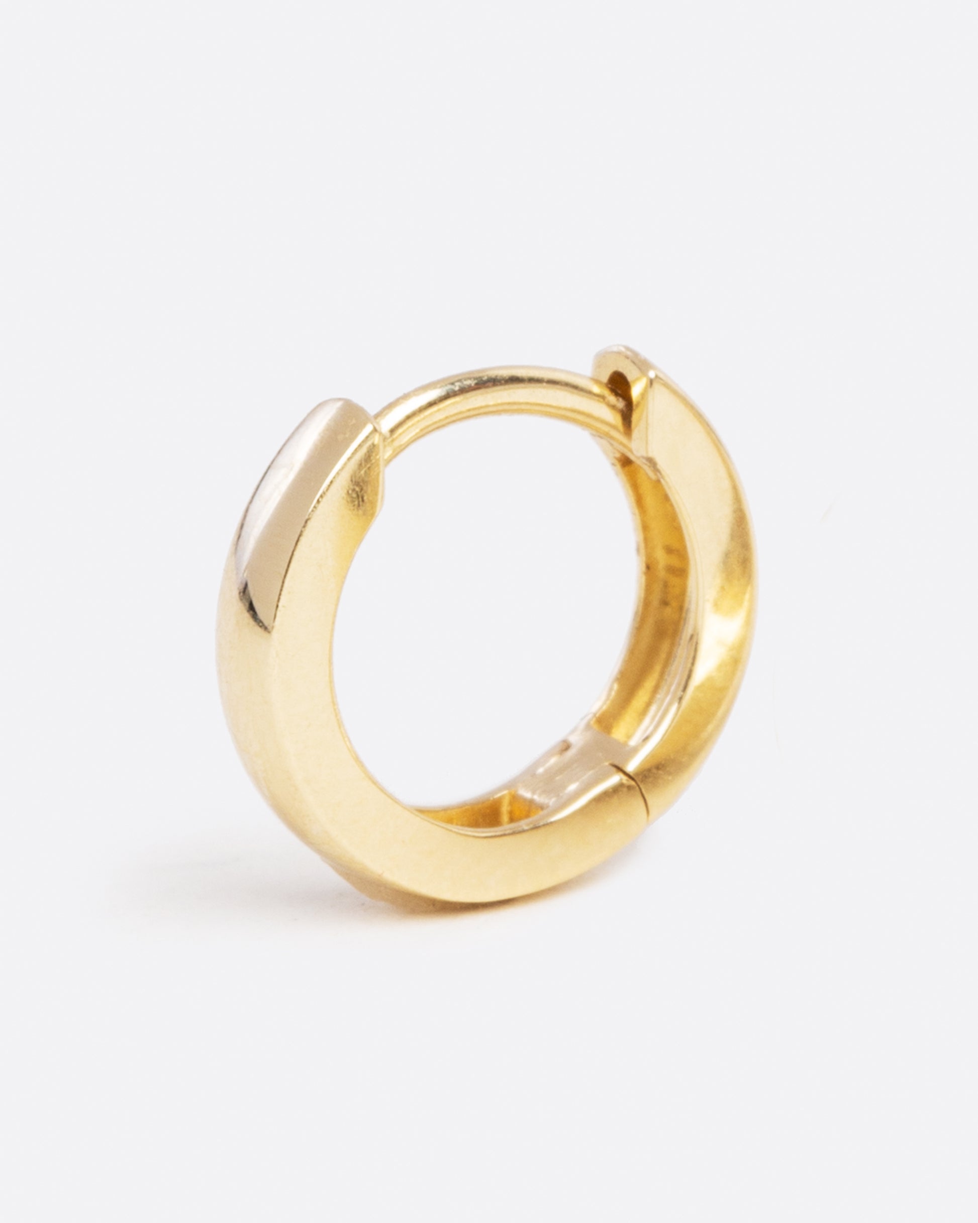a tiny yellow gold hoop earring with a hinge in the middle, shown closed