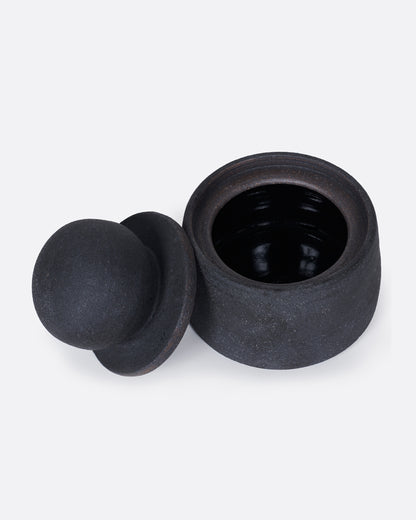 A black jar with a globe lid, shown from above with the lid off and leaning on the jar's side.