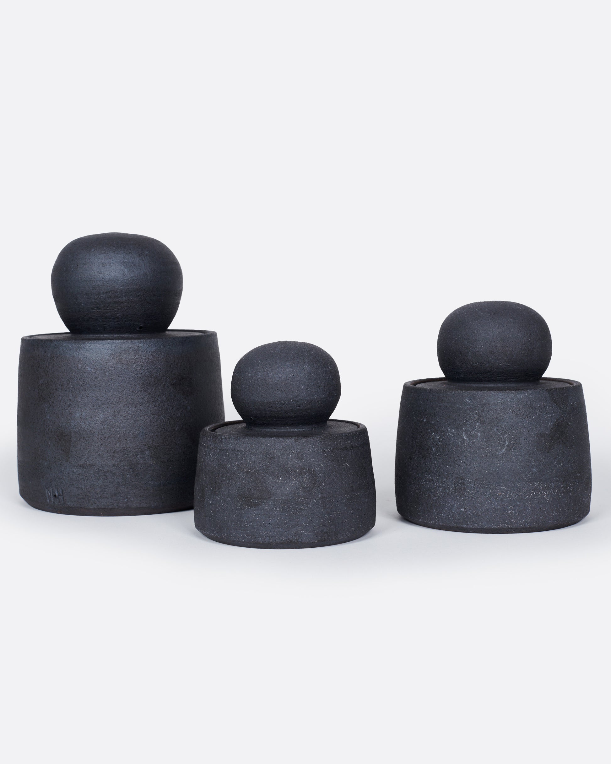 A group of three black jars with globe lids, shown from the front.