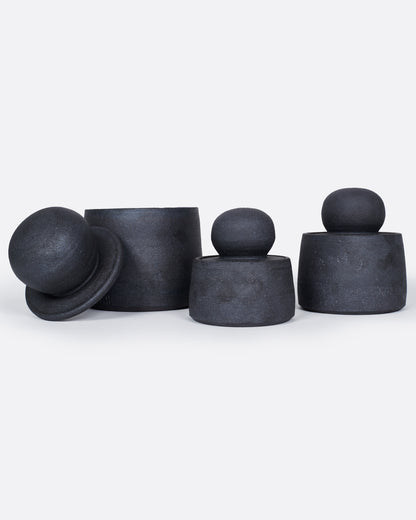 A group of three black jars with globe lids. One jar is open with the lid leaning against its side. Shown from the front.
