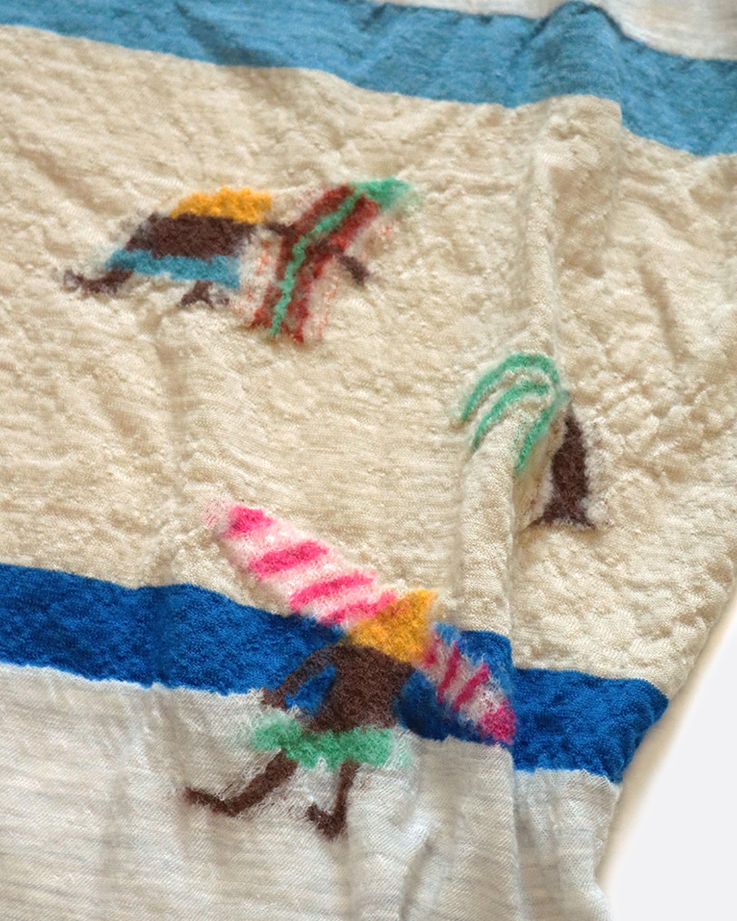 A compressed wool scarf with a fun pattern of surfers on a sandy beach.