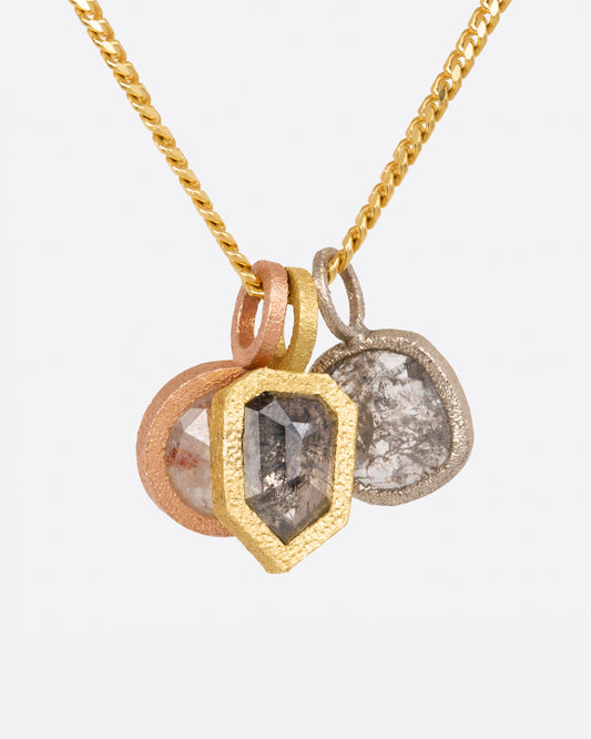A group of three diamond pendants; one in yellow gold, one in rose gold and one in white gold, all hanging on a yellow gold chain.