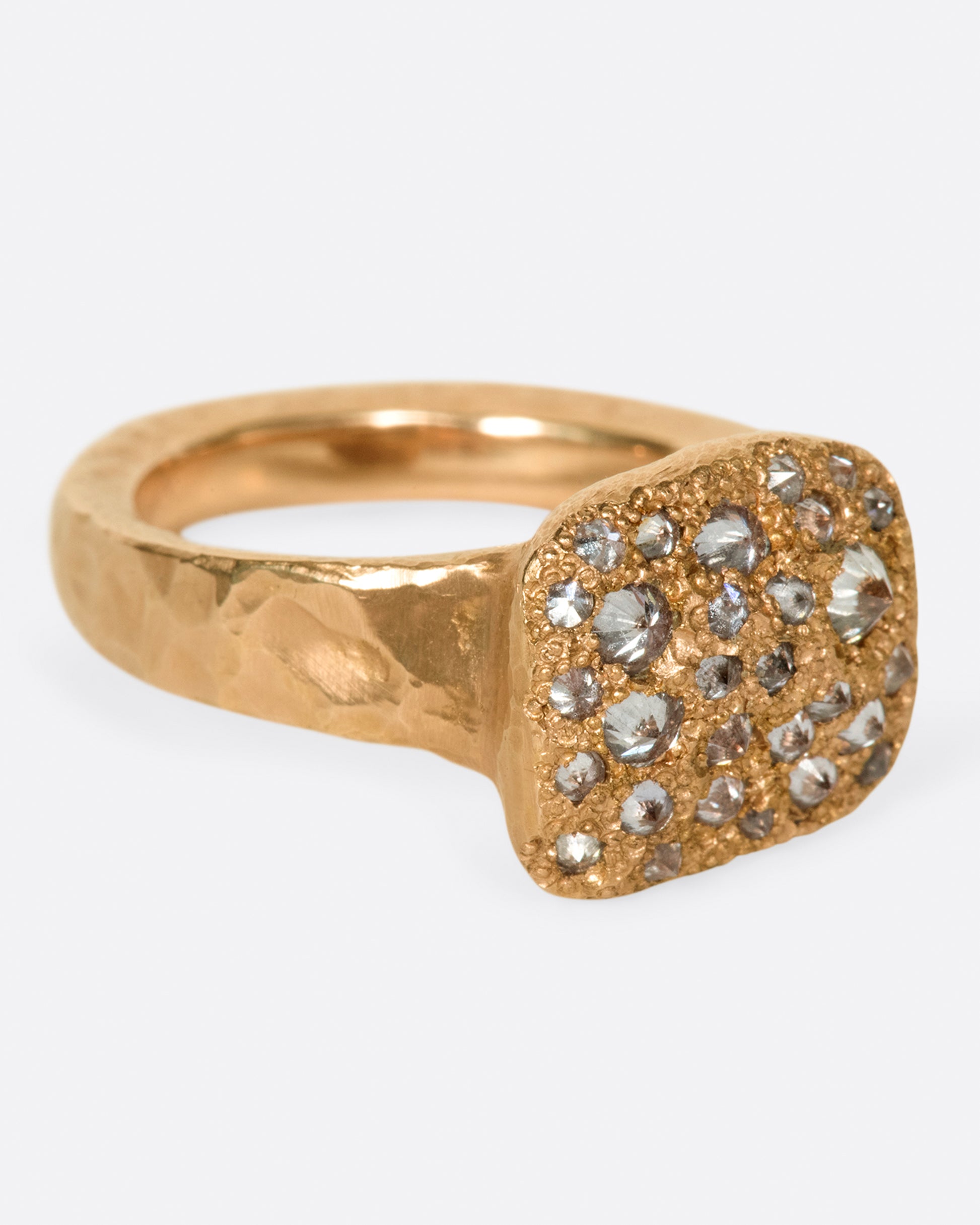 A hammered, hefty rose gold ring with inverted diamonds scattered across its rectangular face.