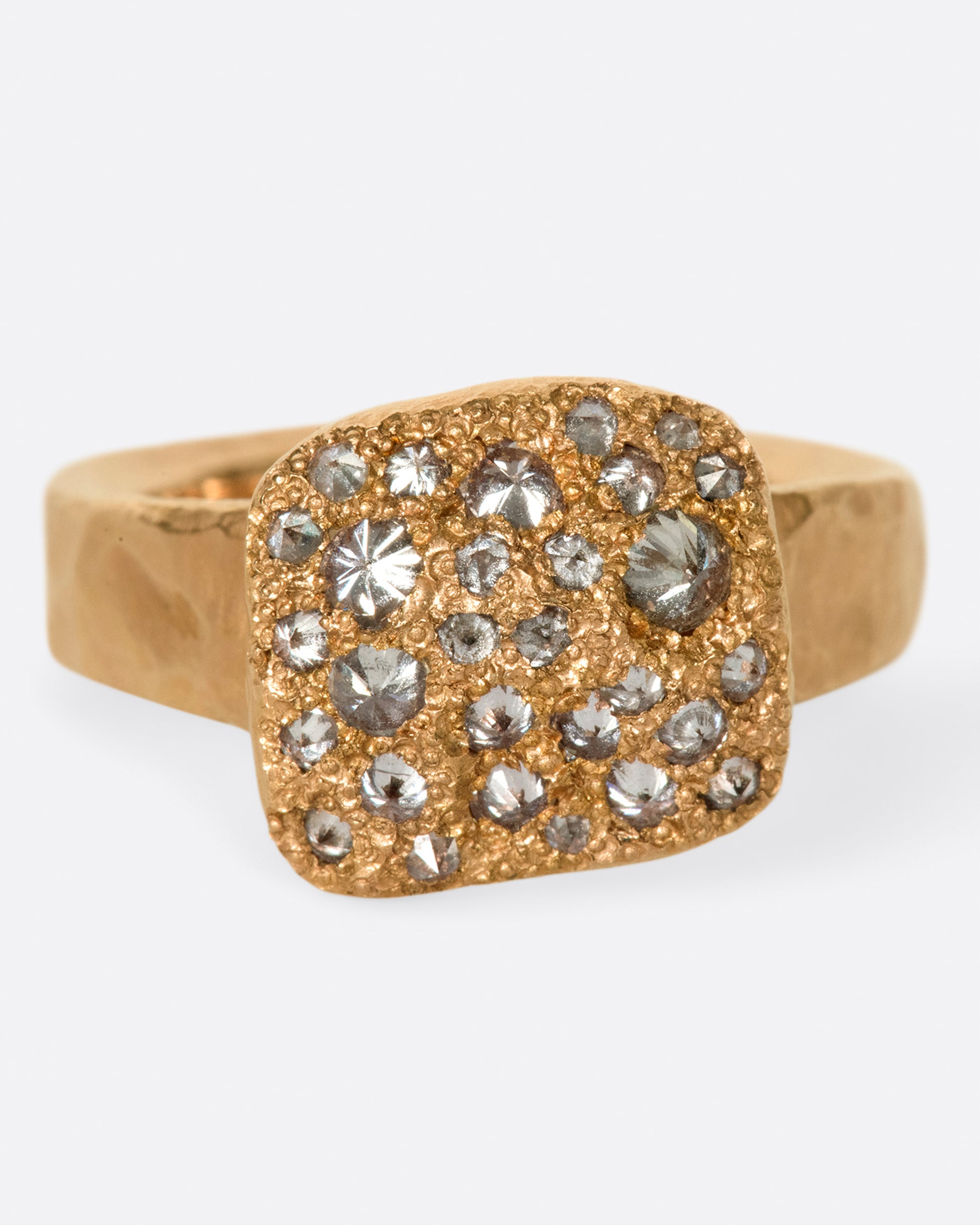 A hammered, hefty rose gold ring with inverted diamonds scattered across its rectangular face.