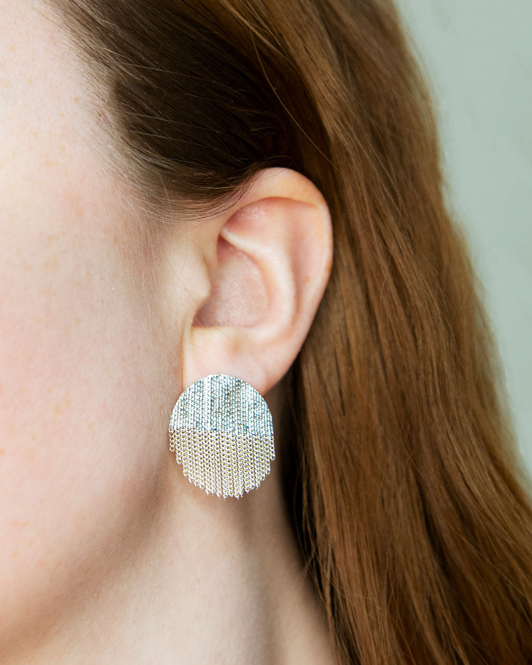 a womans ear with the circle stud on it. it sits close to the ear, with about .75 inches of the earring hanging below the lobe.