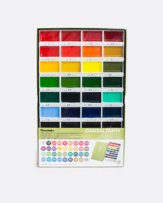 birds eye view of our gansai tambi watercolor set showing a grid of  4 columns and 9 rows of watercolor pans arranged in rainbow order. pictured in packaging with brand note obscuring most of the last 3 rows