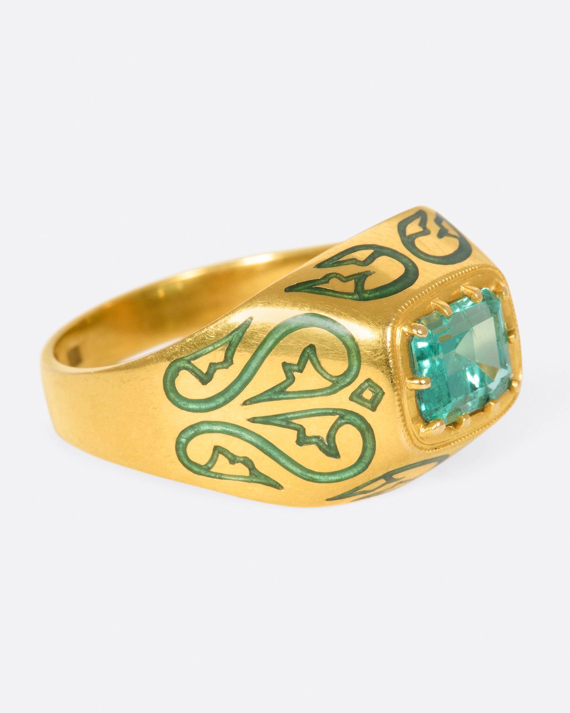 A gold ring featuring a bright Colombian emerald at its center and matching enamel details.