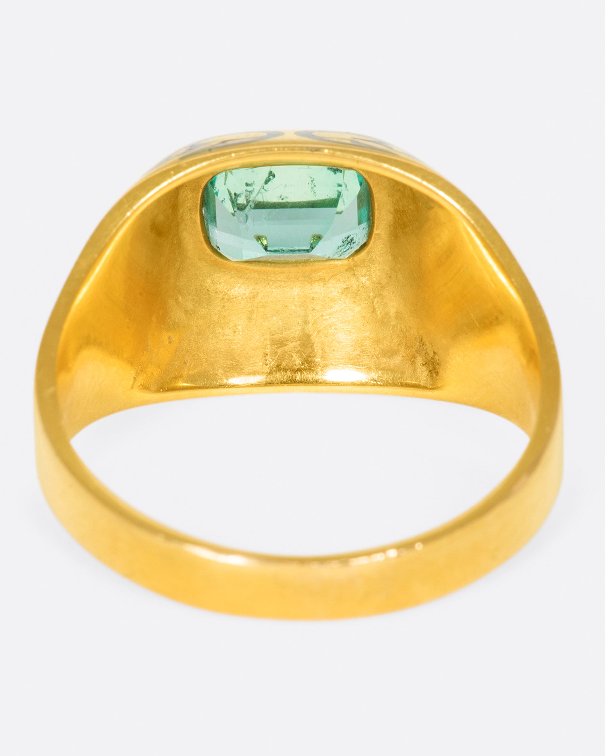 A gold ring featuring a bright Colombian emerald at its center and matching enamel details.