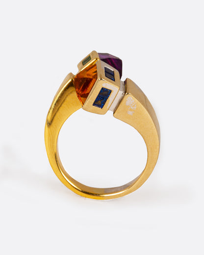 A meld of yellow and white gold, this open wrap ring is tipped with citrine, amethyst, sapphires, and emeralds. The band narrows at the back. Shown standing up from the front.