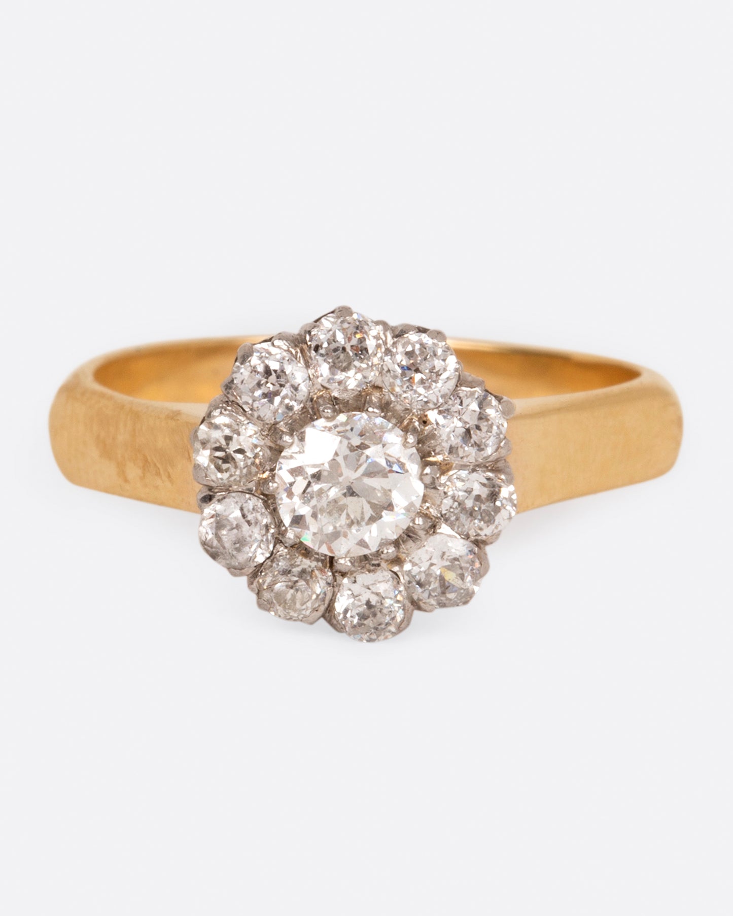 A wide flat yellow gold ring with a flower-shaped cluster of diamonds, shown from the front.
