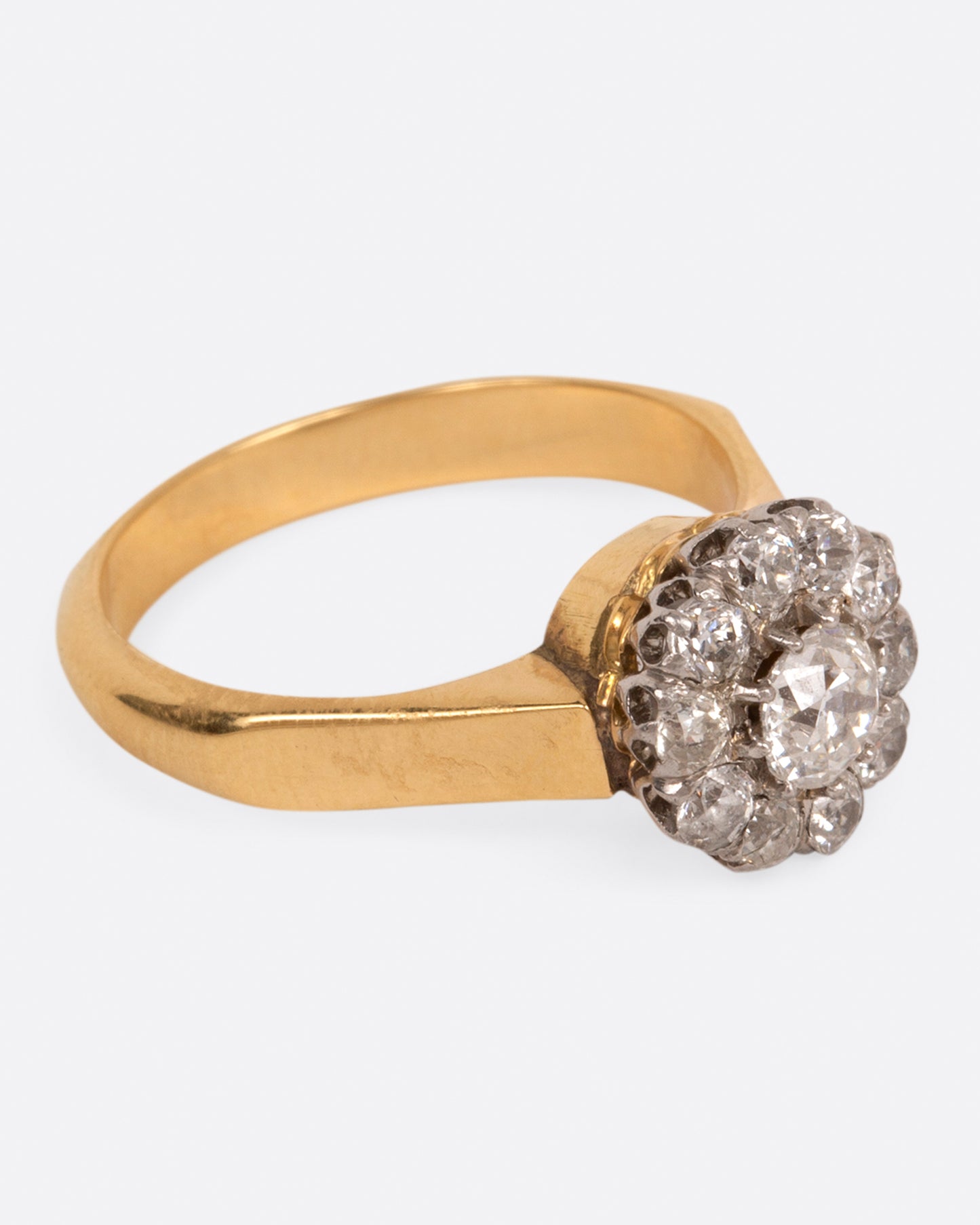 A wide flat yellow gold ring with a flower-shaped cluster of diamonds, shown from the side.