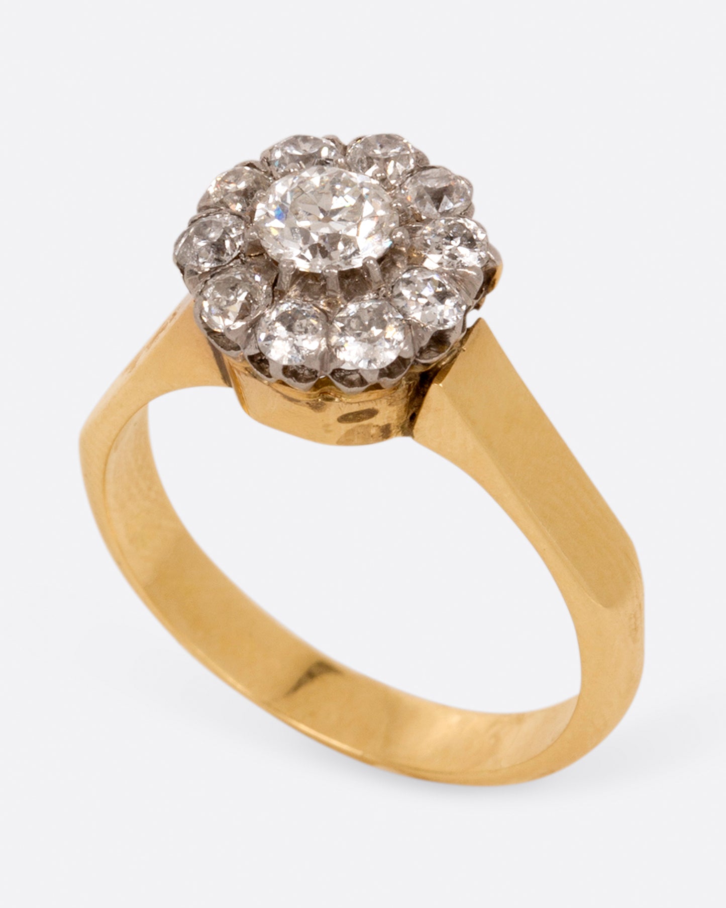 A wide flat yellow gold ring with a flower-shaped cluster of diamonds, shown standing from the side.