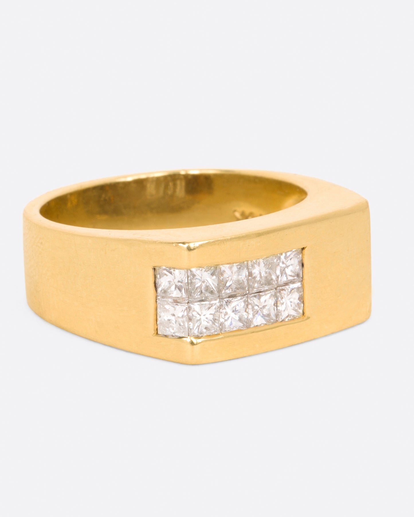A yellow gold rectangular signet ring with 10 princess cut diamonds on one corner, shown from the side.