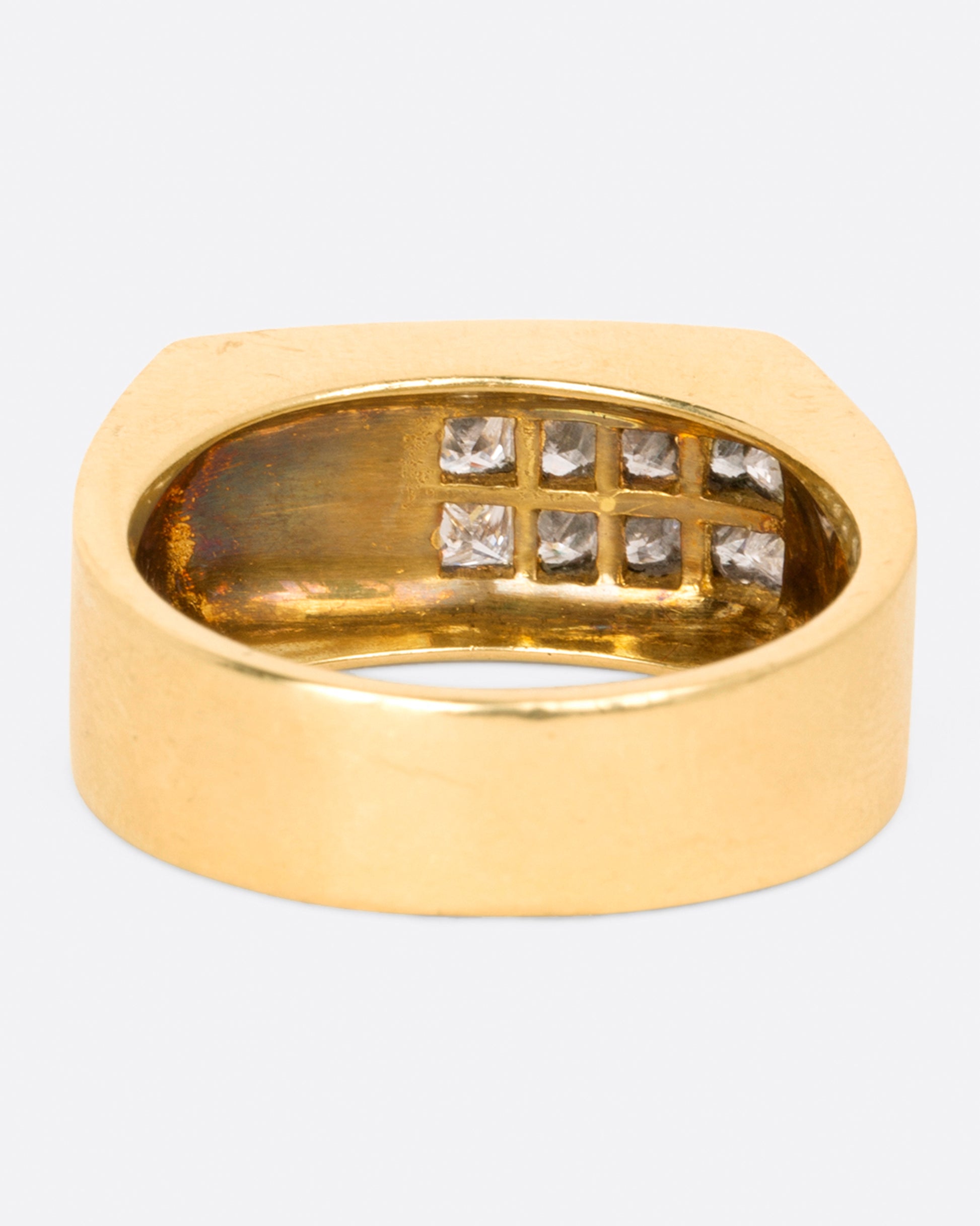 A yellow gold rectangular signet ring with 10 princess cut diamonds on one corner, shown from the back.