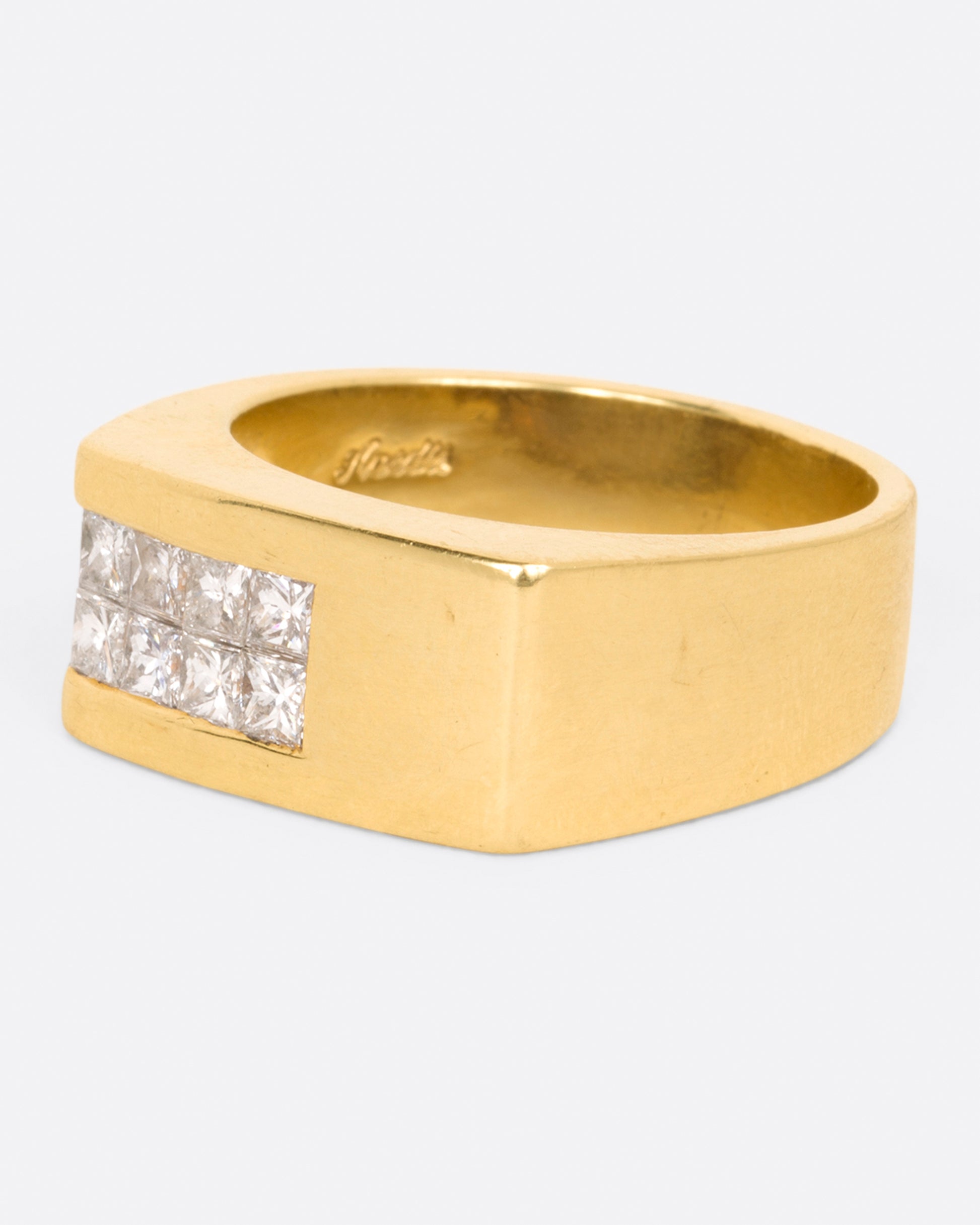 A yellow gold rectangular signet ring with 10 princess cut diamonds on one corner, shown from the side.
