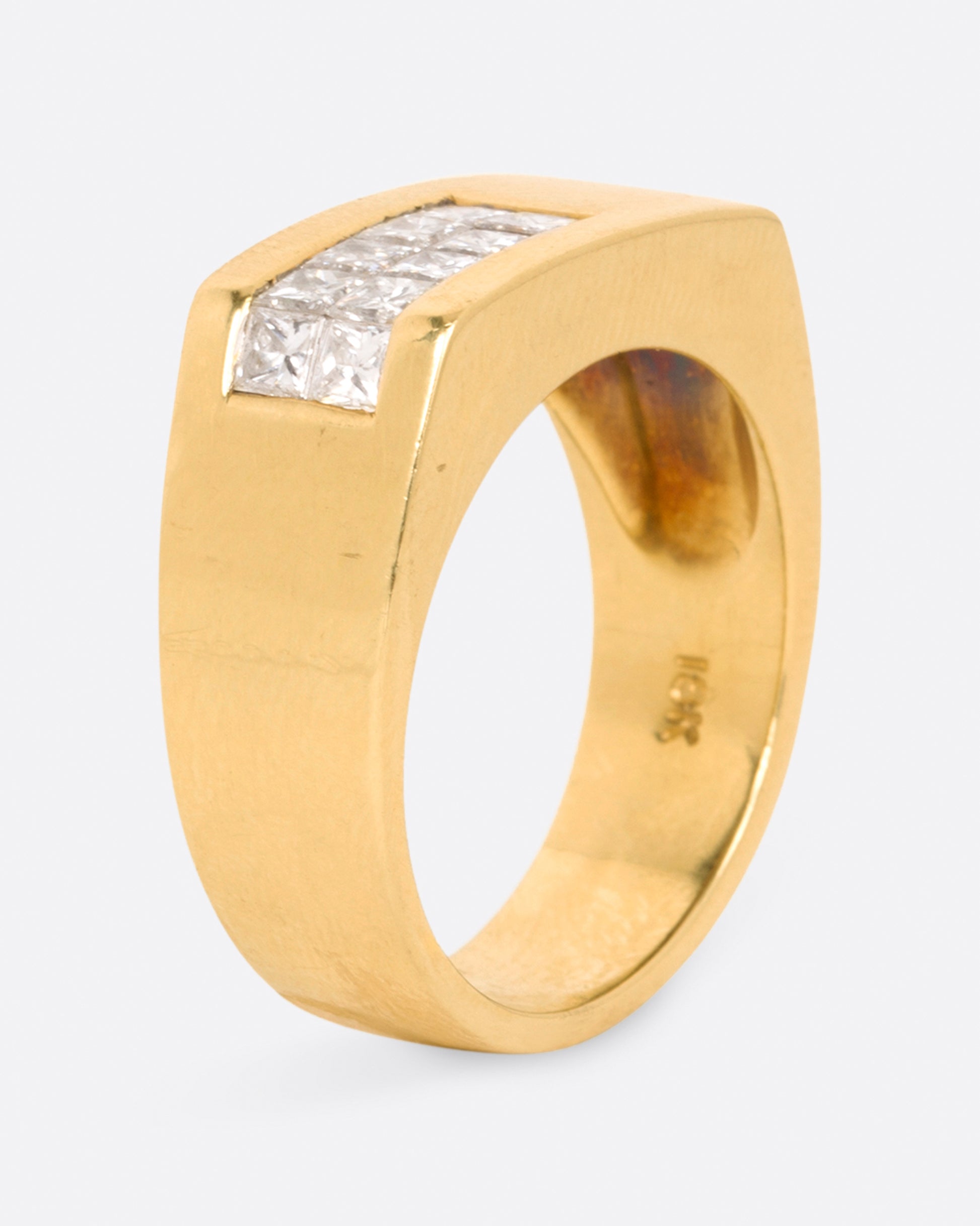 A yellow gold rectangular signet ring with 10 princess cut diamonds on one corner, shown standing up, from the side.