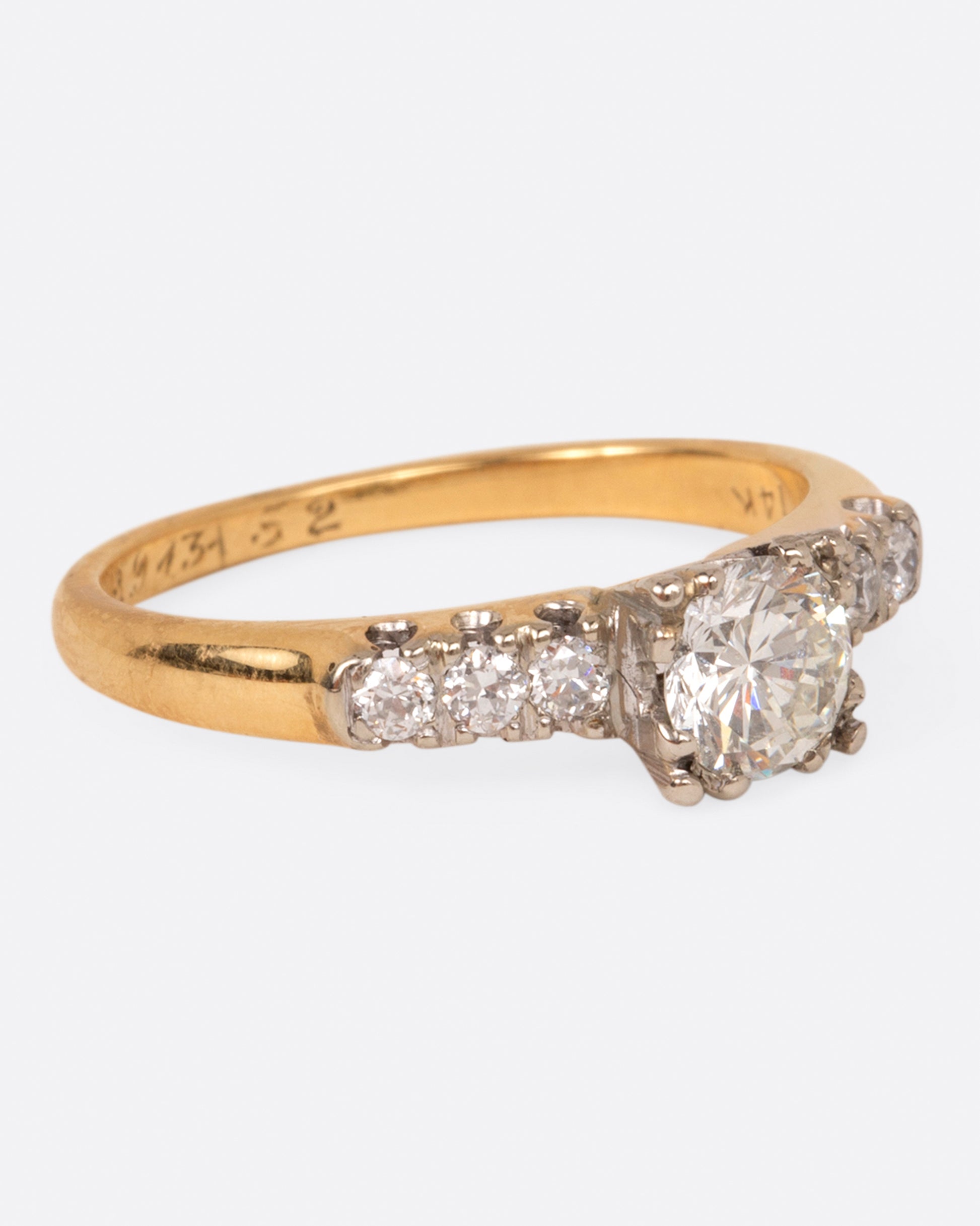 A yellow gold ring with a round center diamond and three smaller round diamonds on either side set in white gold prongs, shown from the side.