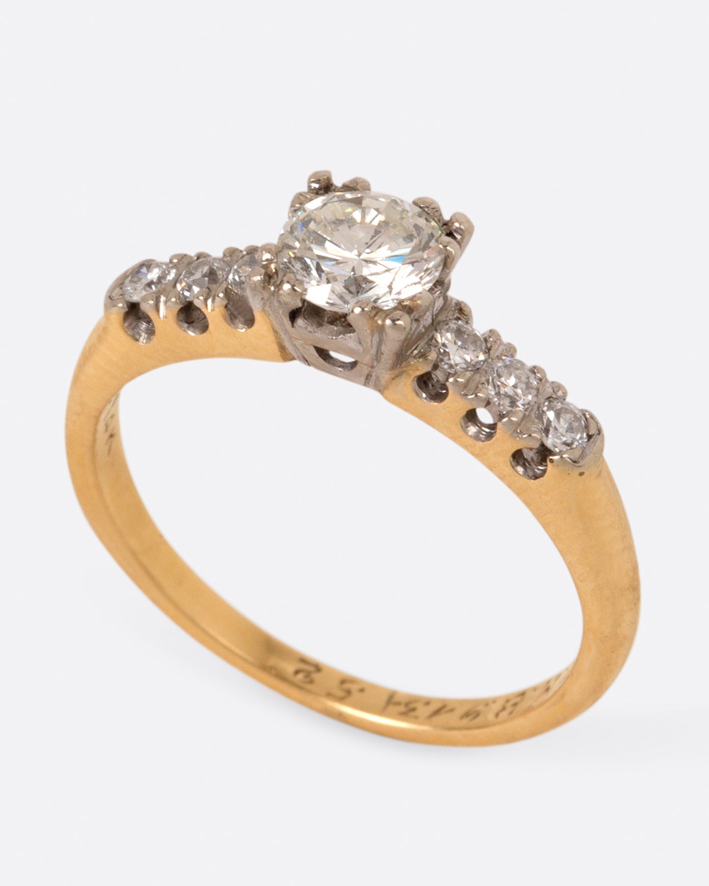 A yellow gold ring with a round center diamond and three smaller round diamonds on either side set in white gold prongs, shown standing.