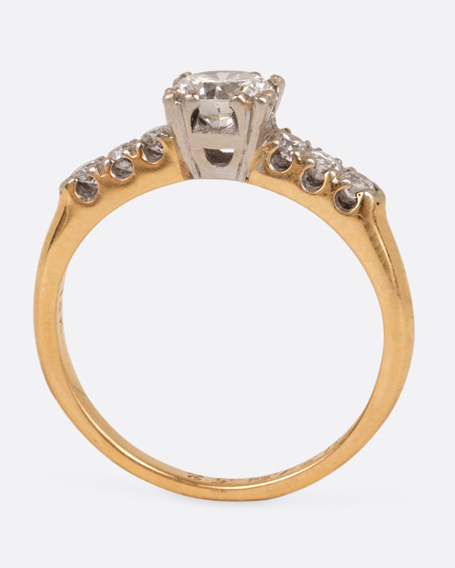 A yellow gold ring with a round center diamond and three smaller round diamonds on either side set in white gold prongs, shown standing.