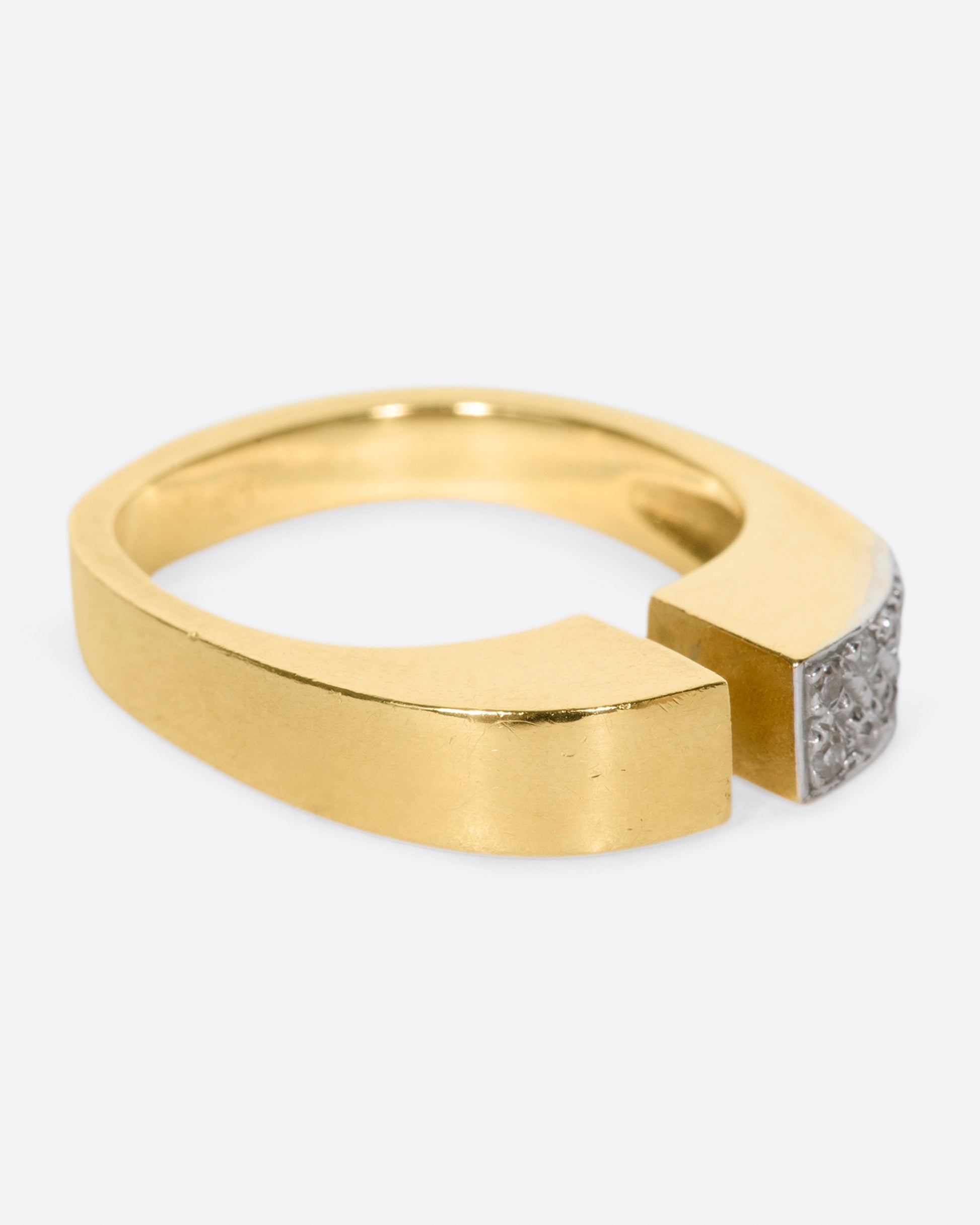 A raised, open, yellow gold ring with one pavé diamond corner.