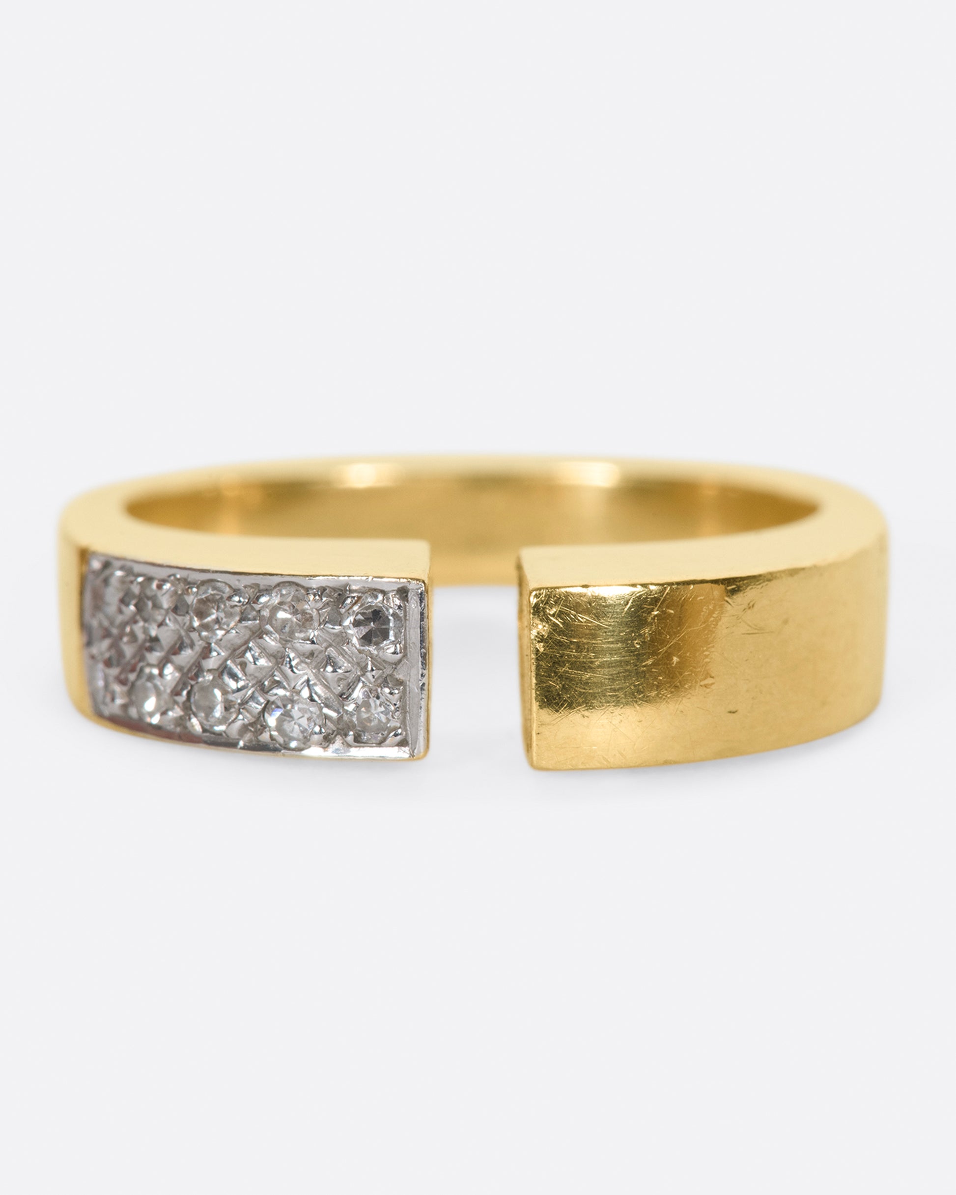 A raised, open, yellow gold ring with one pavé diamond corner.