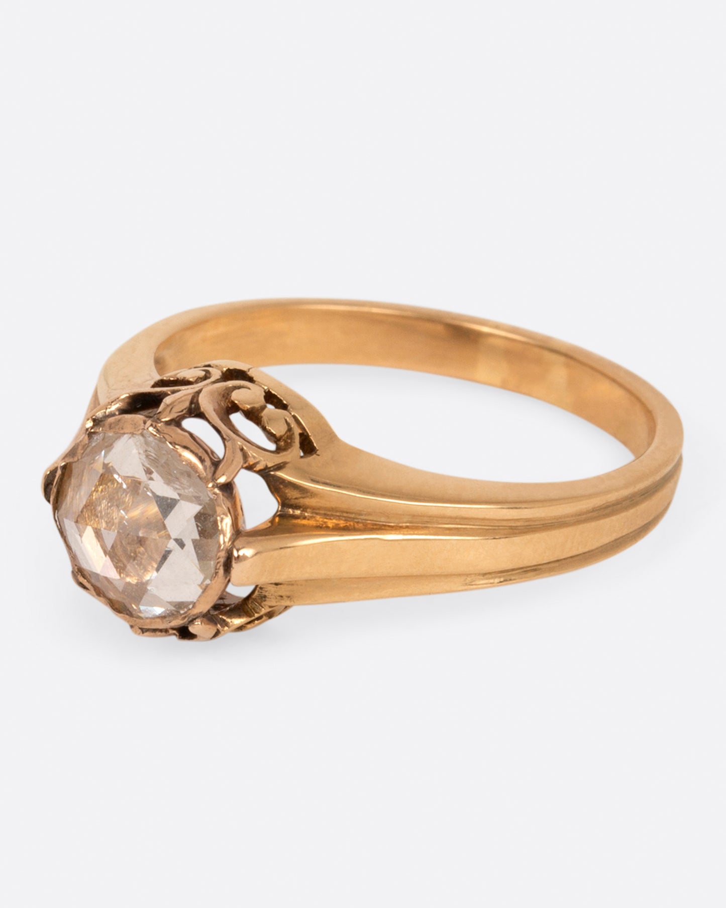 A yellow gold diamond solitaire ring with a rose cut diamond and a ribbed band, shown from the side.