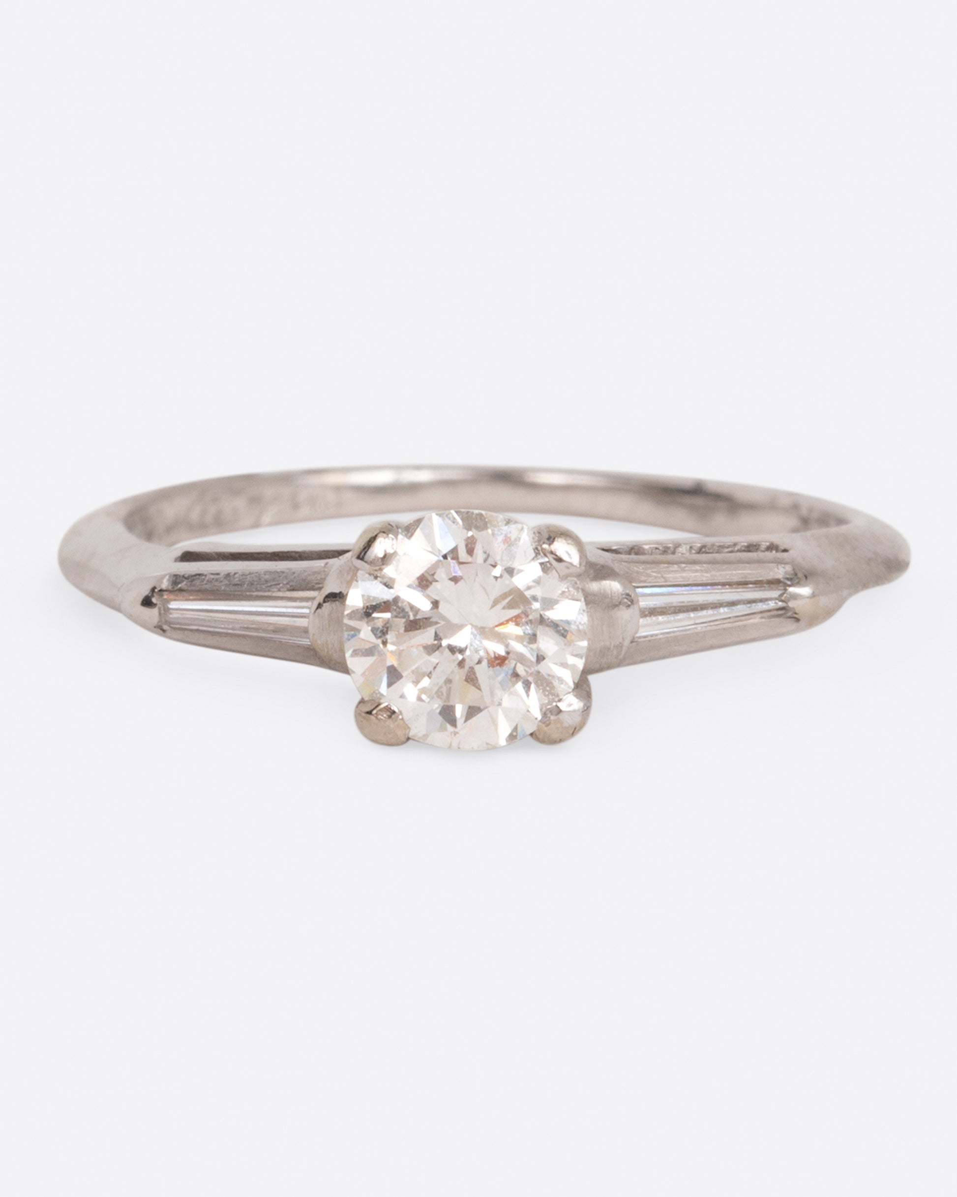 A white gold ring with a round prong-set diamond at the center and tapered baguette diamonds on either side, shown from the front.