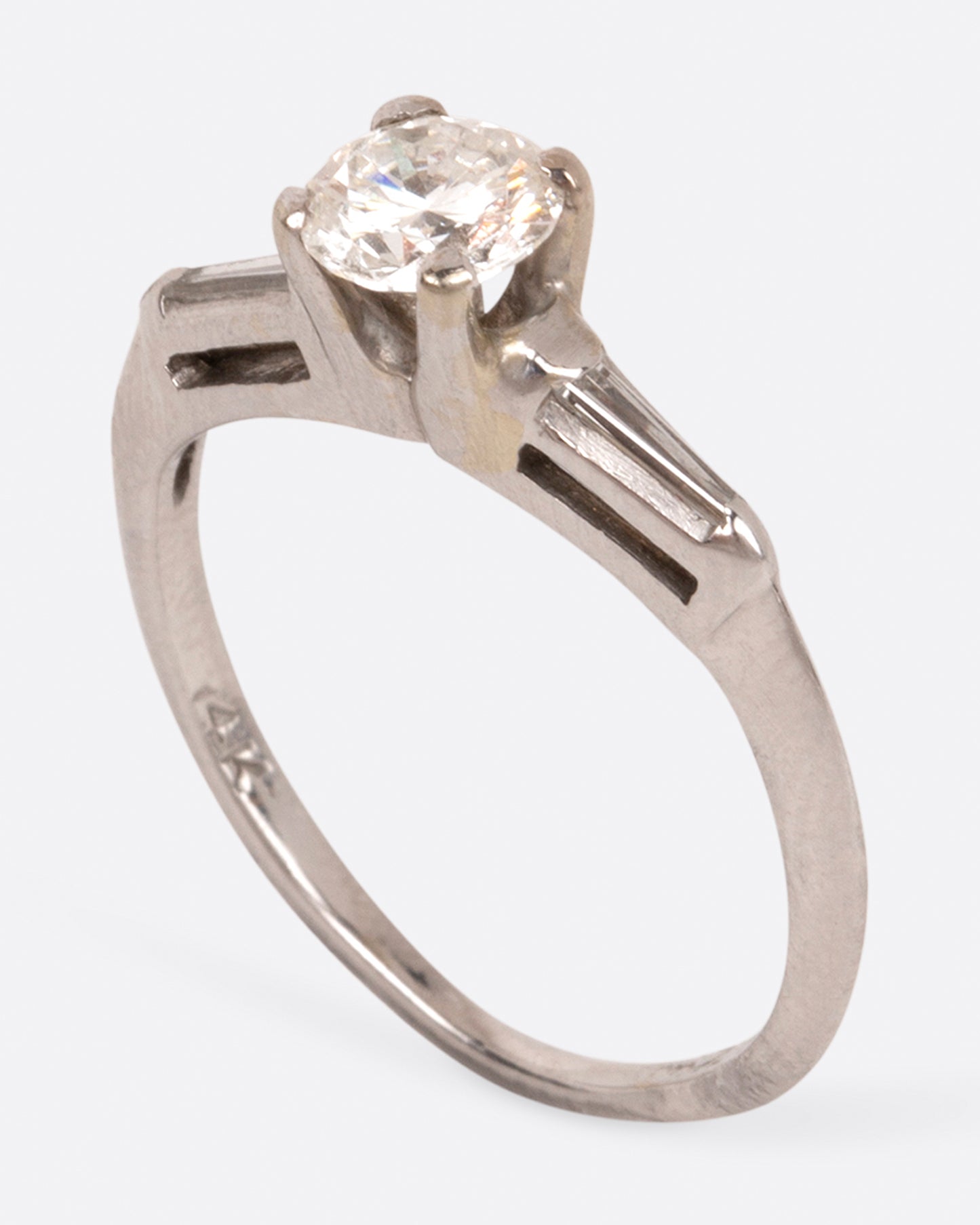 A white gold ring with a round prong-set diamond at the center and tapered baguette diamonds on either side, shown standing.