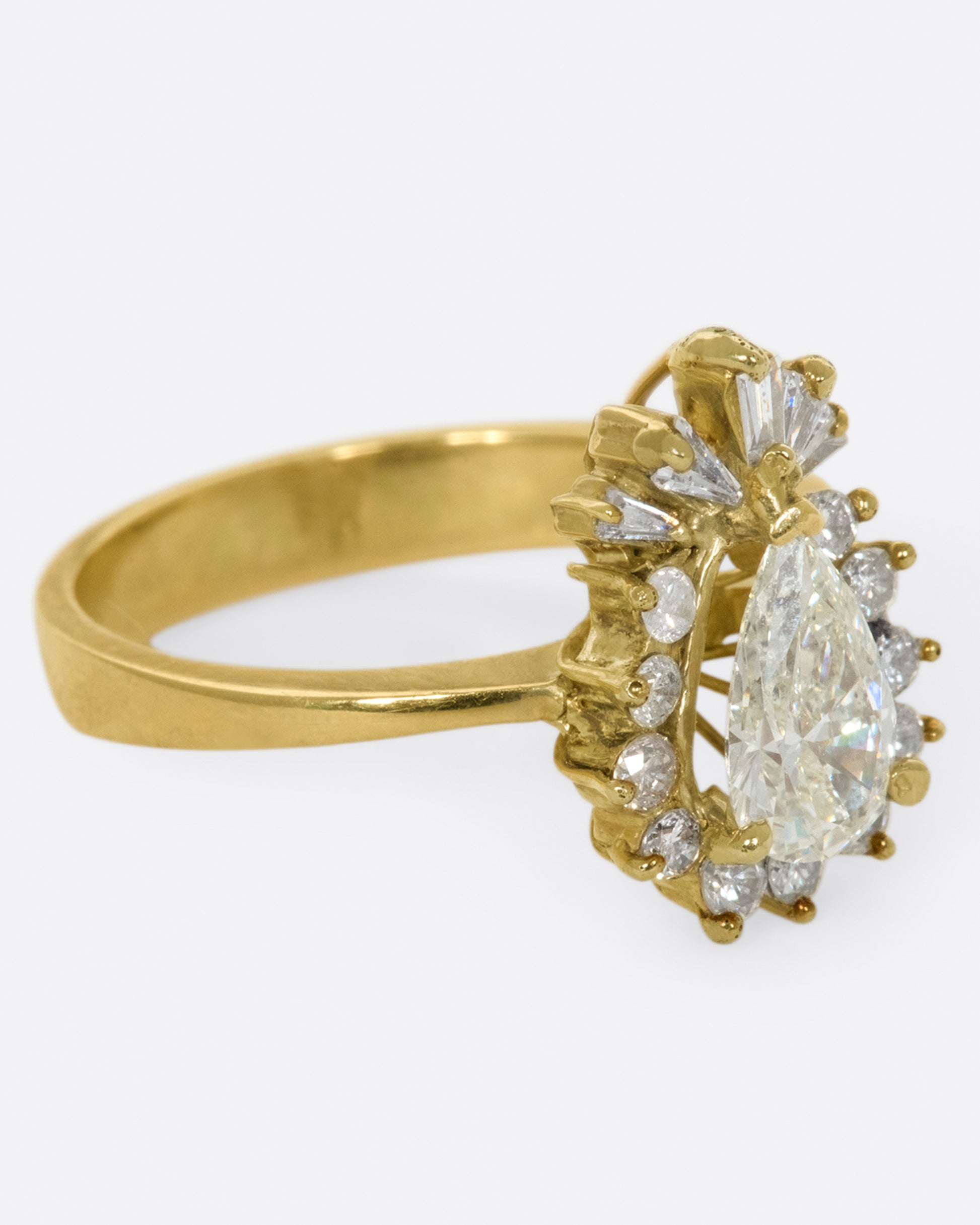 A tapered ring with a pale yellow, pear shaped diamond at its center with a round and baguette diamond halo.