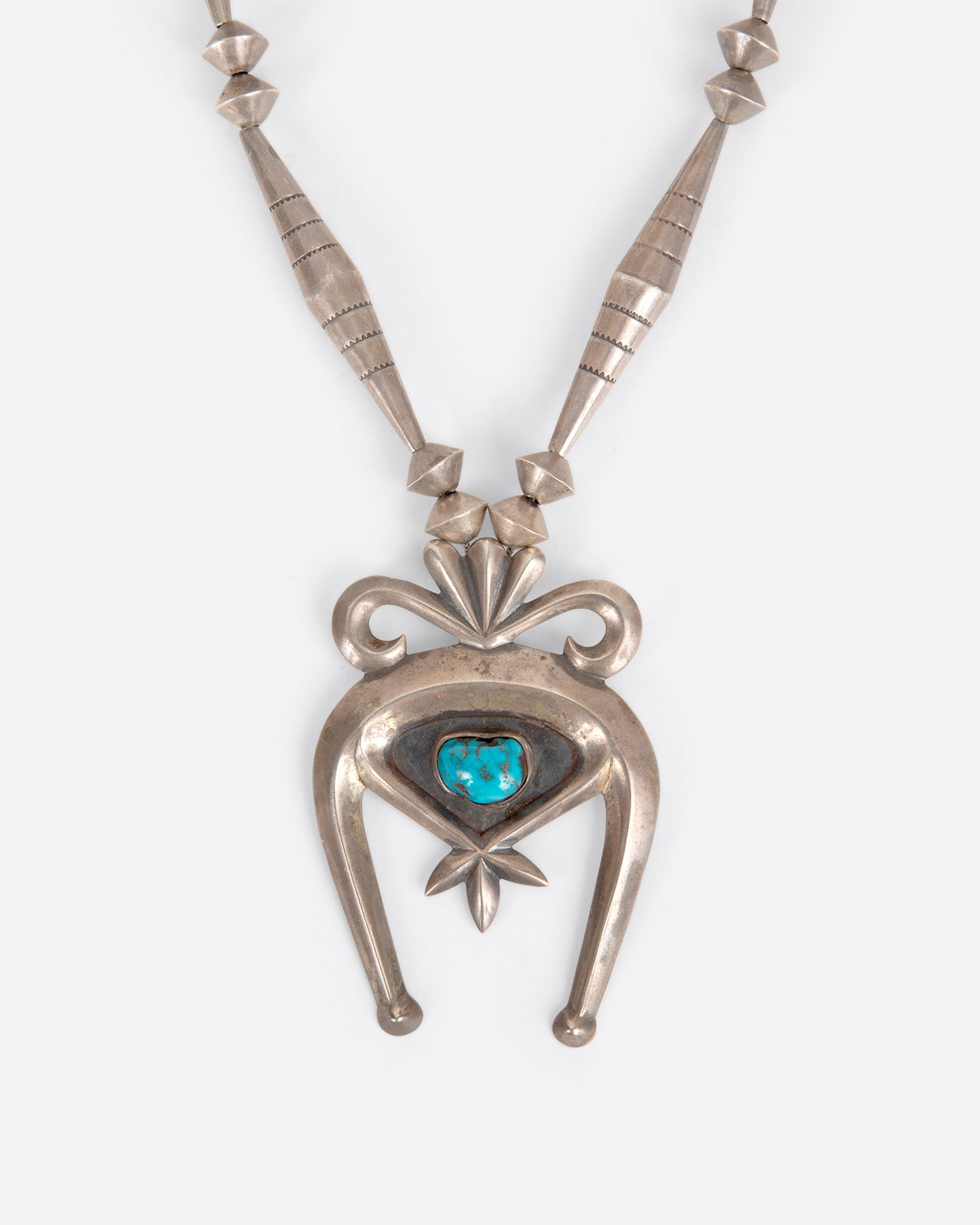 A vintage silver naja necklace with a turquoise stone at the center of the pendant, shown from the front.