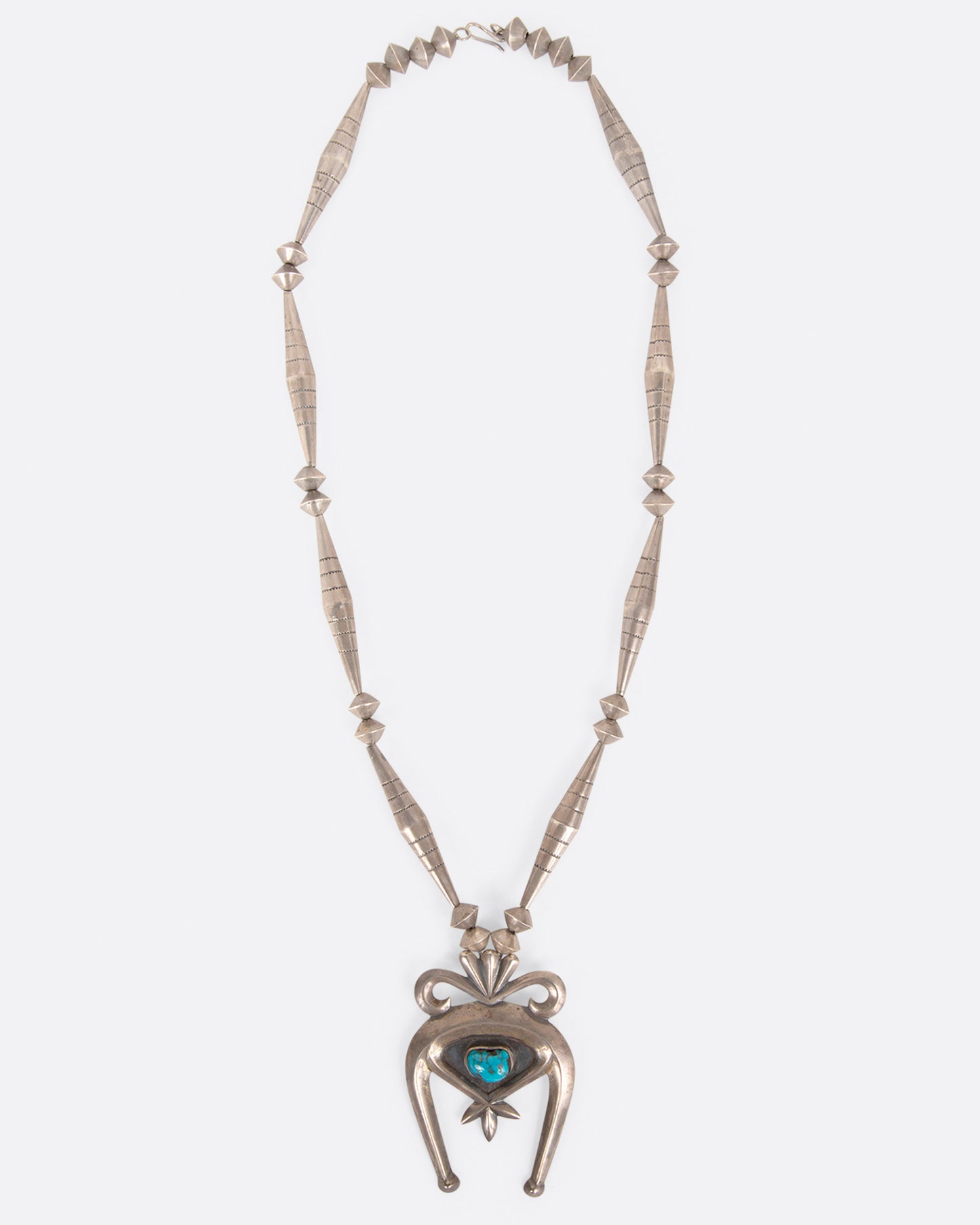 A vintage silver naja necklace with a turquoise stone at the center of the pendant, shown from above.
