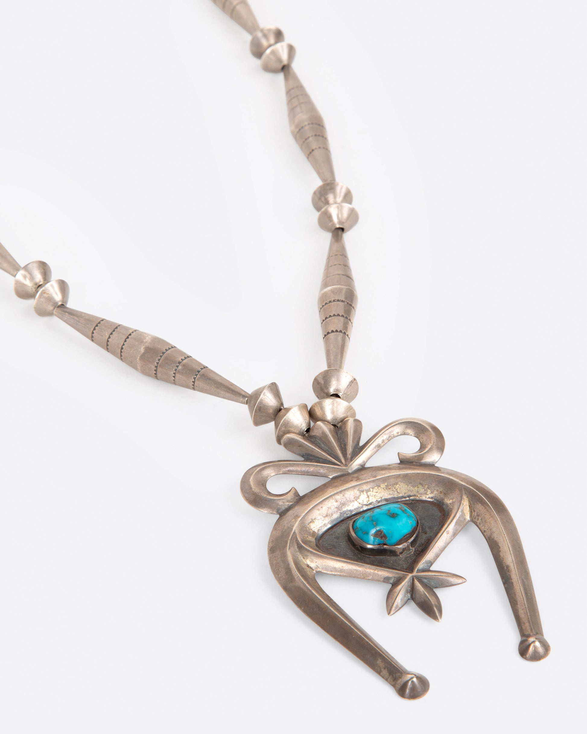 A vintage silver naja necklace with a turquoise stone at the center of the pendant, shown from the side.